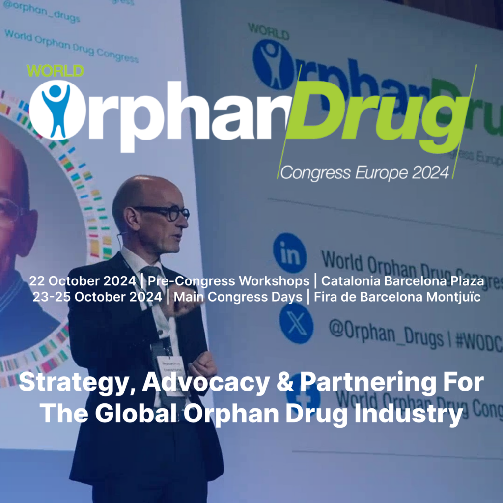 Ponente en el escenario del World Orphan Drug Congress Europe 2024, con el logo del evento y detalles en la pantalla que incluyen las fechas y la ubicación: '22 de octubre 2024, talleres precongreso en Catalonia Barcelona Plaza' y '23 al 25 de octubre 2024, jornadas principales en Fira de Barcelona Montjuïc'. Texto destacado en la imagen: 'Estrategia, defensa y colaboración para la industria global de medicamentos huérfanos'.